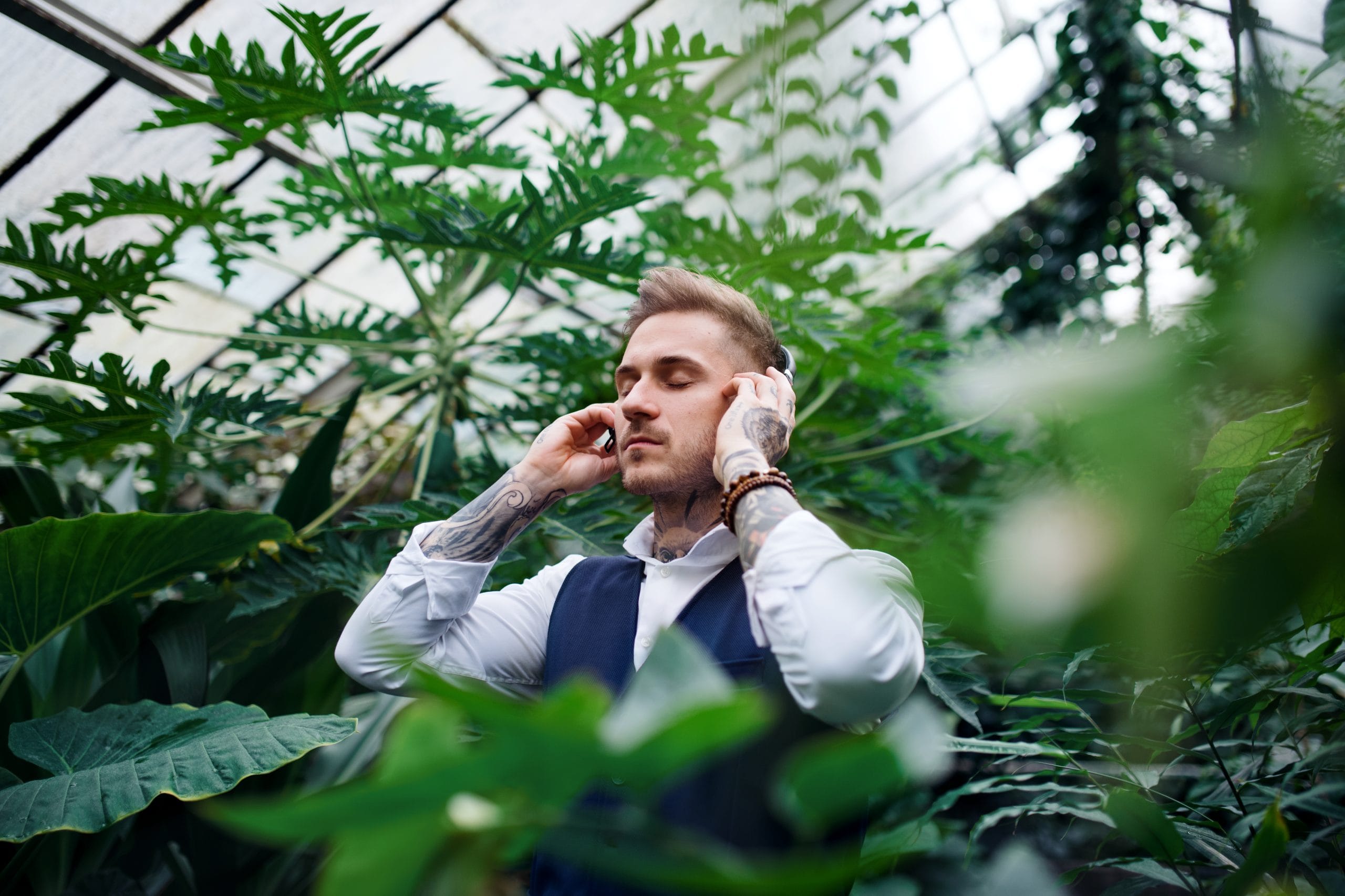 Young man with headphones standing in botanical garden