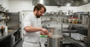 Rene Redzepi cooking in a stainless steel pot.